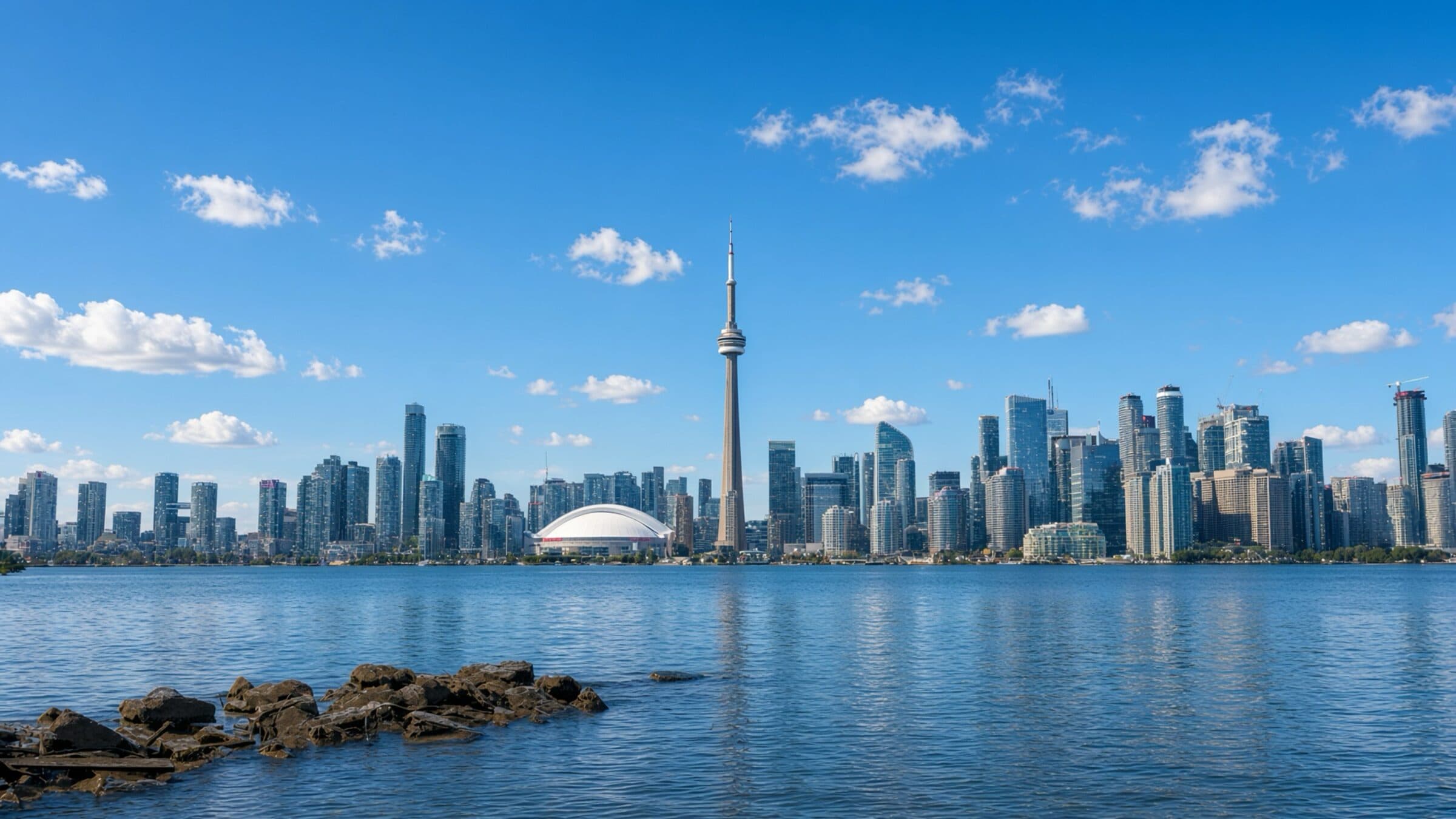 The Toronto skyline under a clear blue sky, the CN Tower at its centre, seen across Lake Ontario